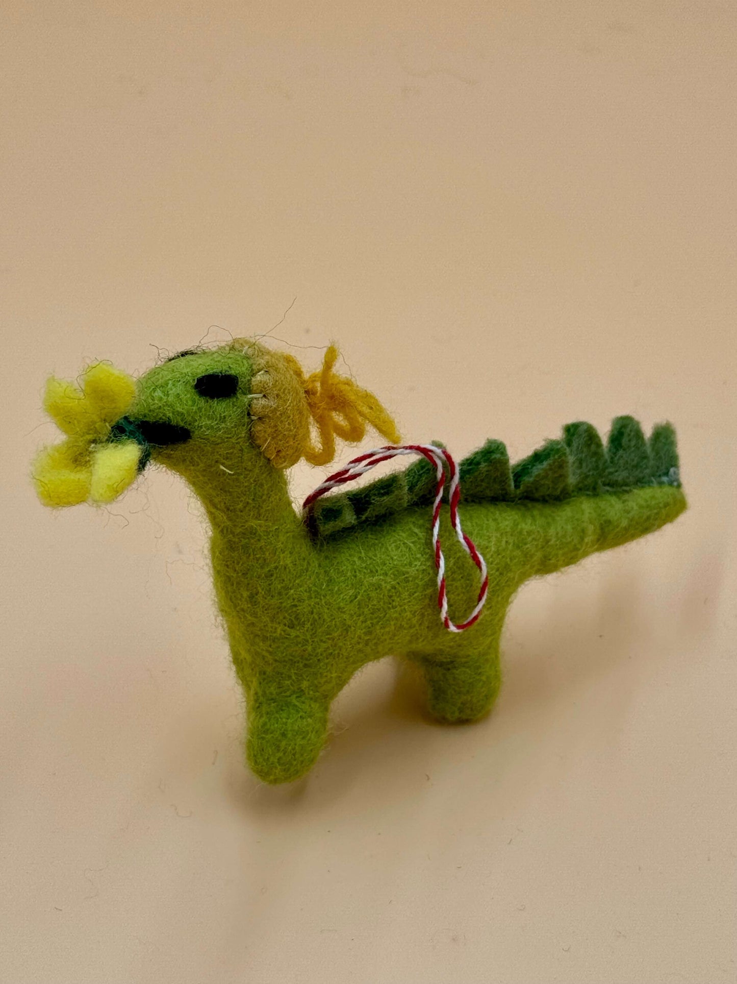 Filzanhänger Schlüsselanhänger Dino mit Blume, handgemacht aus Wolle, grün mit gelben Blütendetails.
