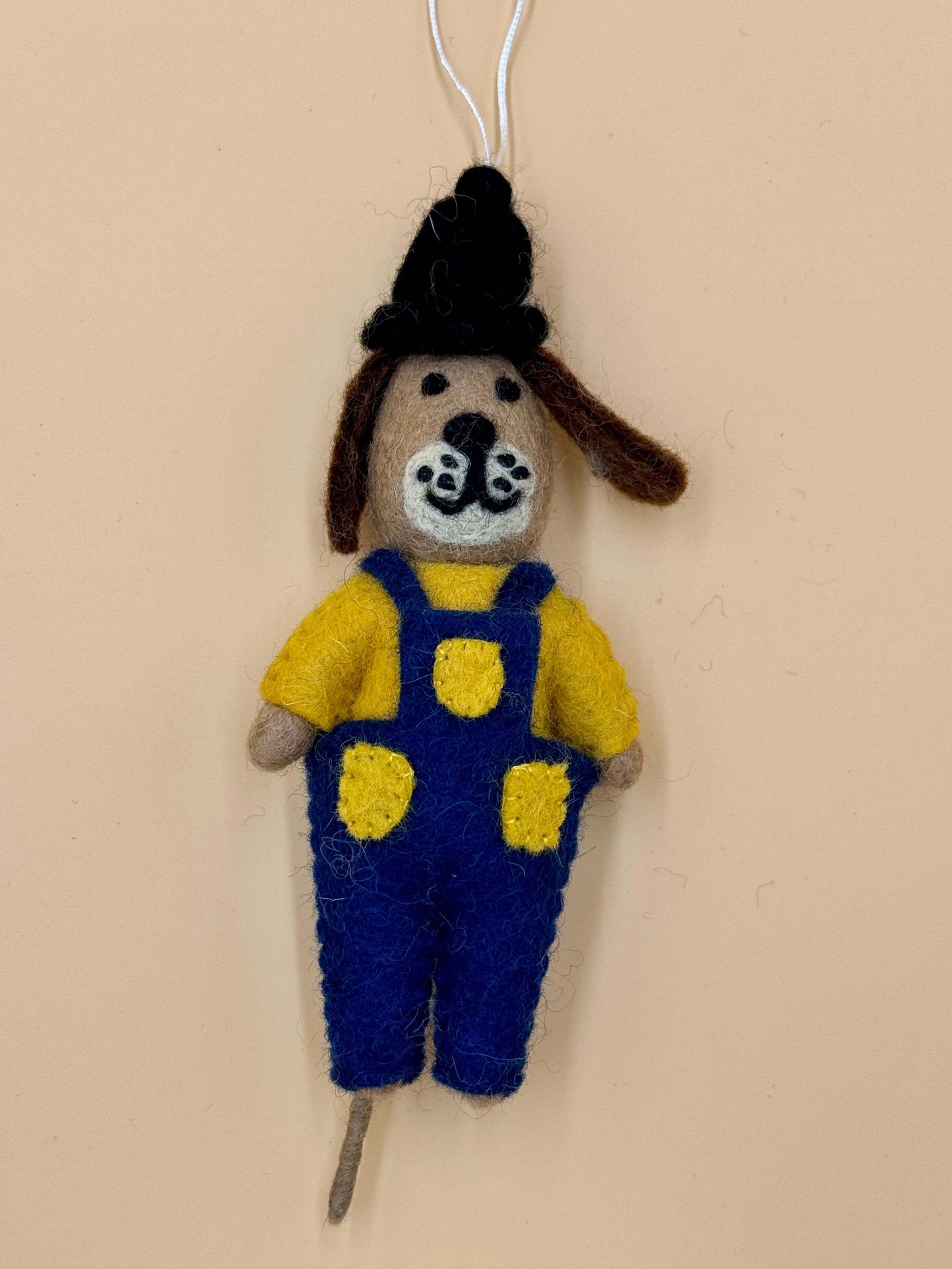 Handgemachter Filzanhänger Schlüsselanhänger in Form eines Hundes mit Mütze und Latzhose in Blau und Gelb.