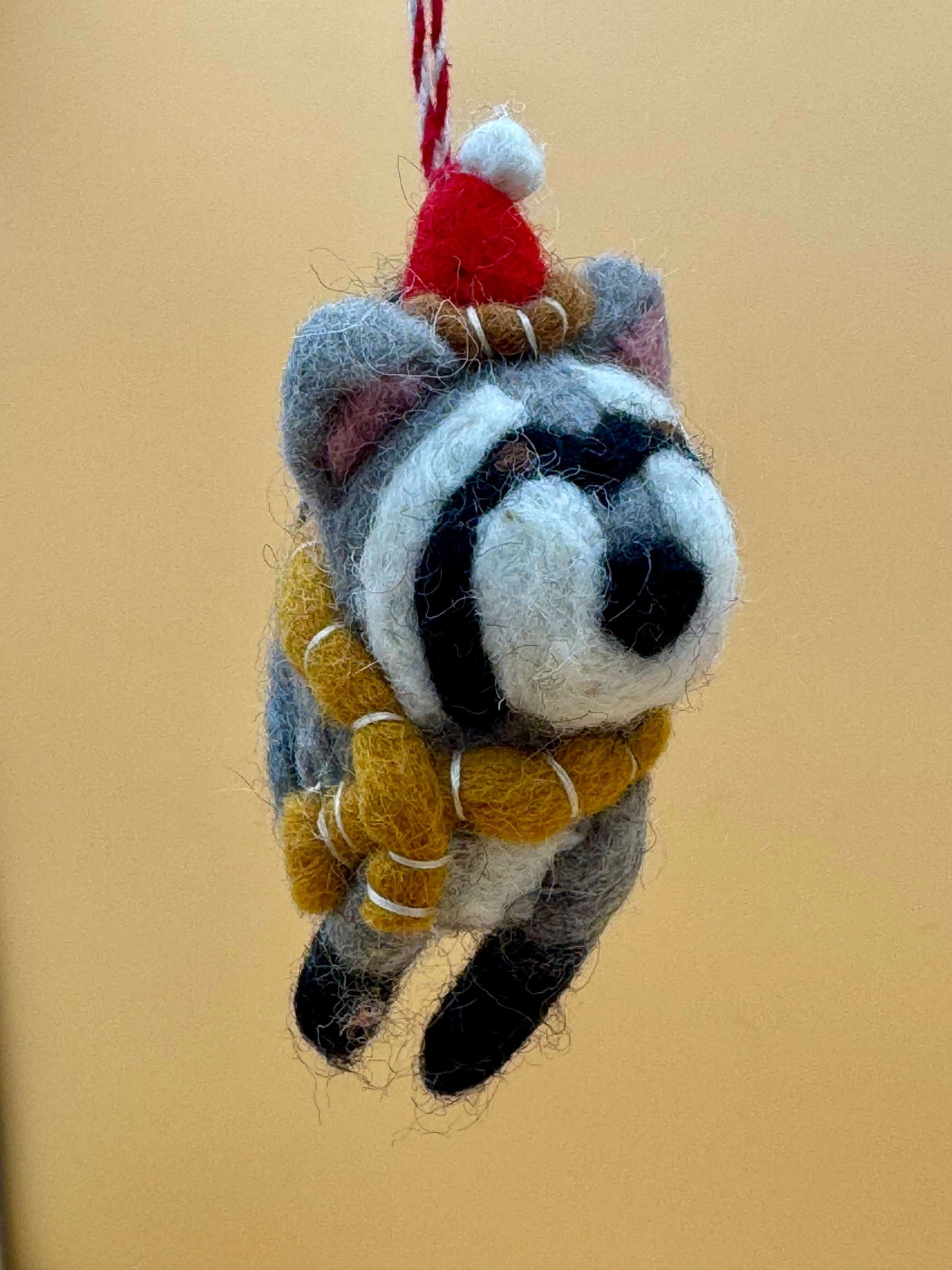 Handmade grey and black felt raccoon keychain with scarf and hat, perfect for Christmas decorations.