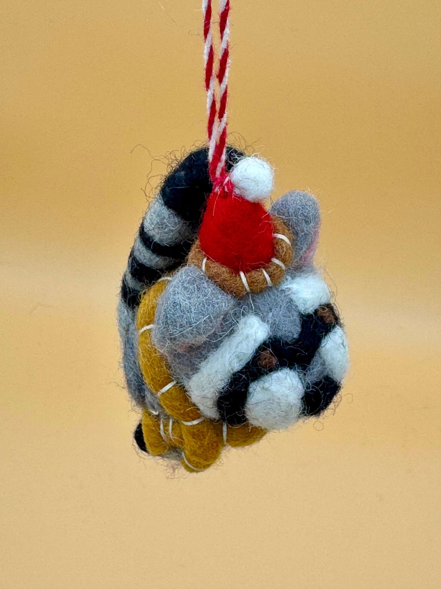 Handgemachter Filzanhänger Weihnachtswaschbär Schlüsselanhänger in grau, schwarz, rot mit Mütze und Schal.