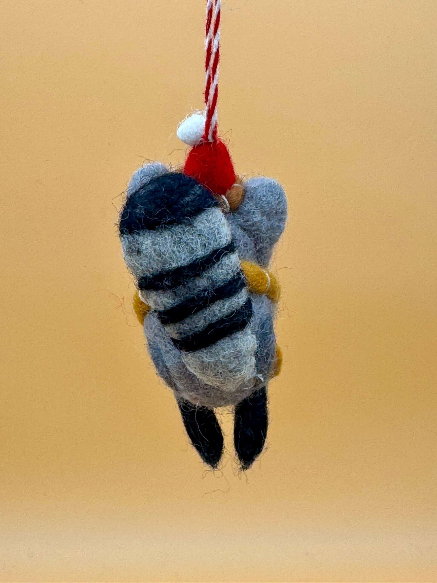 Handgemachter Filzanhänger Schlüsselanhänger Weihnachtswaschbär in grau, schwarz und rot, mit Schal und Mütze.