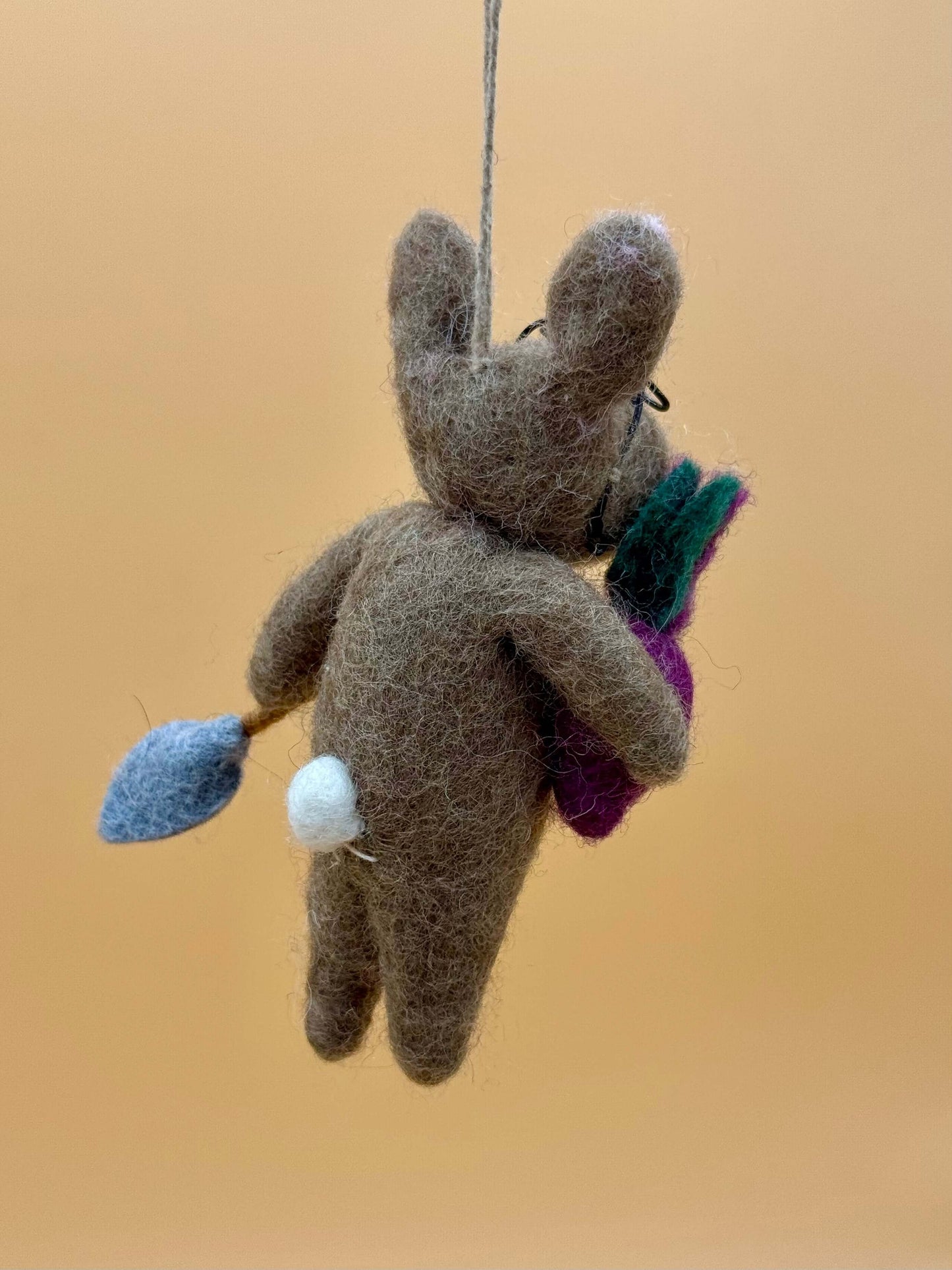 Handmade brown felt rabbit keychain holding a purple vegetable with a blue shovel, unique and crafted from 100% wool.