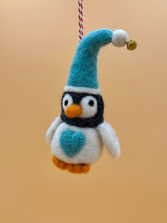 Filzanhänger Schlüsselanhänger Pinguin mit Mütze blau, handgefertigt aus Wolle, fröhliches Design mit orangefarbener Ecke.