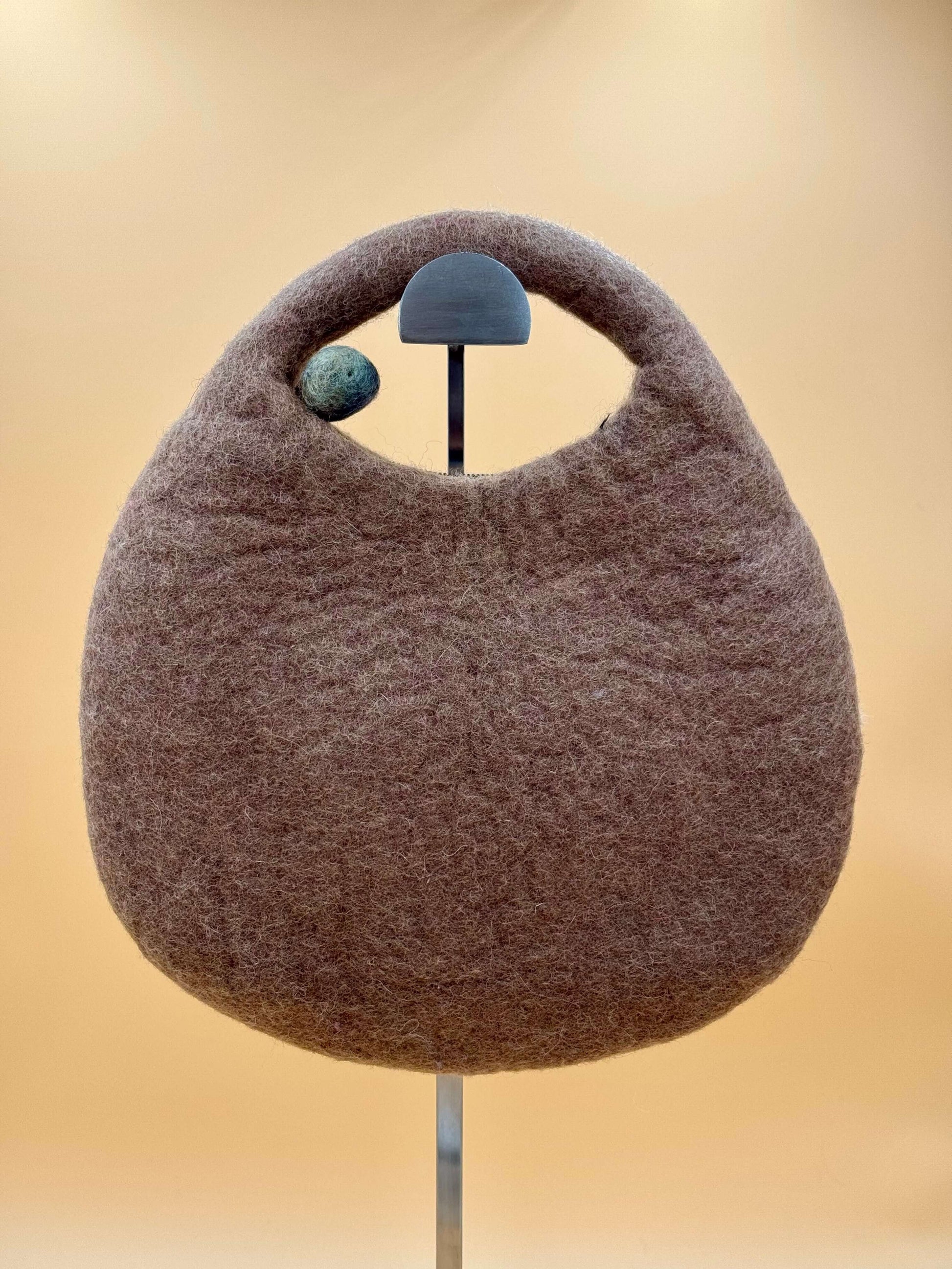 Handmade brown felt saddle bag with a rounded handle, perfect for holding essentials.